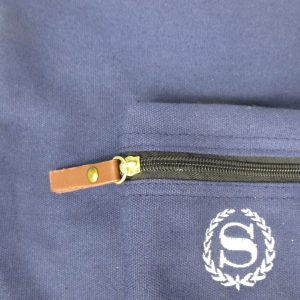 Close-up of brown leather zipper pull and embroidered logo on navy canvas