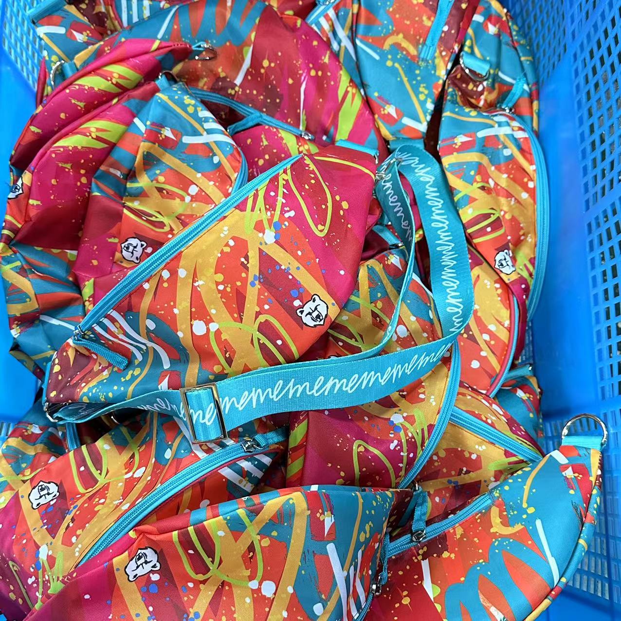 Basket of colorful splash art waist bags with custom printed teal straps