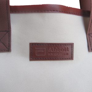 Close-up of embossed Abbott PU label and X-stitched handle on tote bag